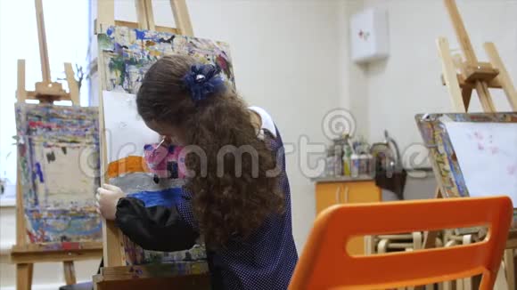 年轻可爱的女艺术家在一个艺术工作室坐在一个Easel和绘画画布绘图过程视频的预览图