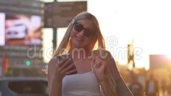 有魅力的年轻女性在耳机里听音乐在城市散步日落环顾四周微笑肖像视频的预览图