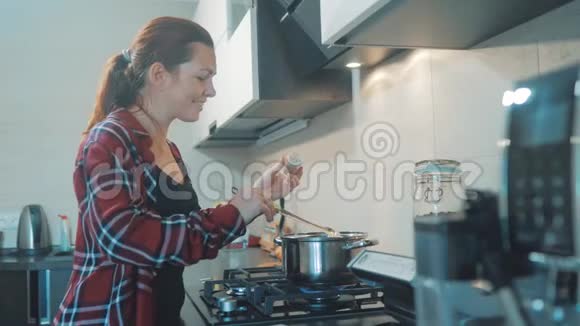 女人在厨房煮汤锅防止锅里的水看看数字平板上的食谱妇女视频的预览图