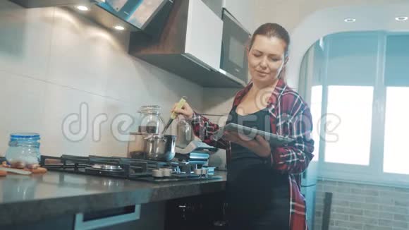 女人在厨房煮汤防止锅中的水看看数字平板上的食谱妇女视频的预览图