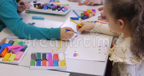 坐在书桌前的可爱的小孩子们在桌子上雕刻出了一与彩色造型塑料制成的不同的图形视频的预览图