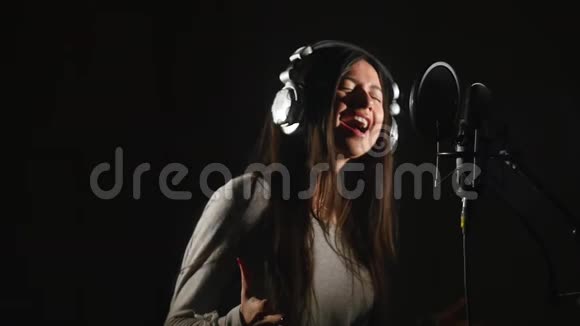 录音室带着耳机和录音室麦克风唱歌的女人视频的预览图