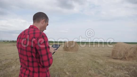 智慧农业理念一位农民在一片田野上研究干草堆研究生活方式一台数字平板电脑慢动作视频的预览图
