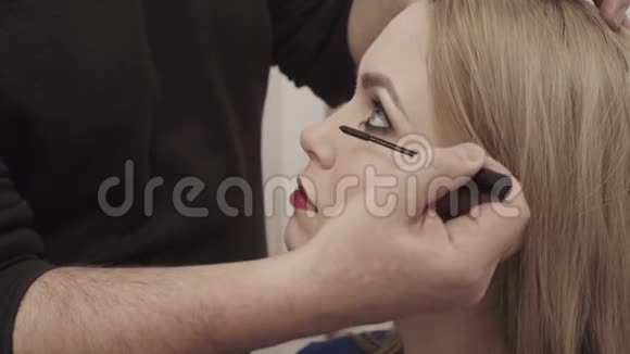 化妆师给一个有魅力的年轻女人化妆为年轻女孩化妆美容院的年轻女孩金发碧眼视频的预览图