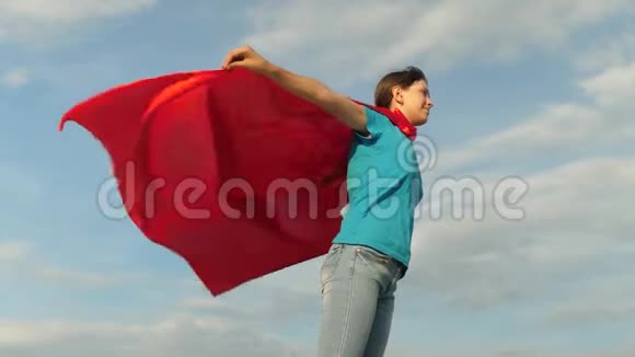 美丽的女孩超级英雄穿着红色斗篷站在田野上斗篷随风飘扬慢动作女孩的梦想视频的预览图