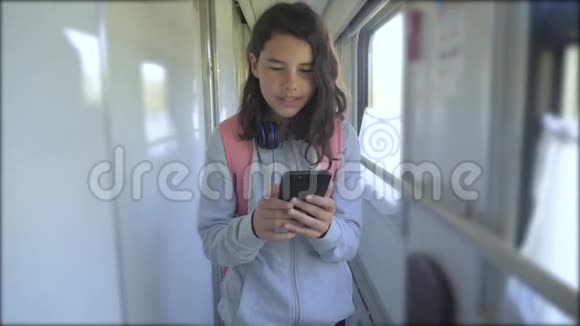 十几岁的女孩带着背包和智能手机在火车车厢里散步旅游运输铁路概念这就是视频的预览图