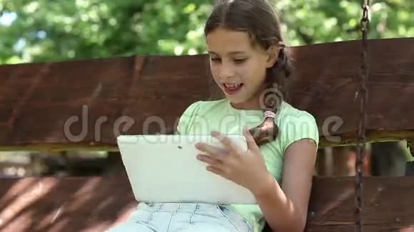 有平板电脑的漂亮女孩坐在秋千凳上视频的预览图