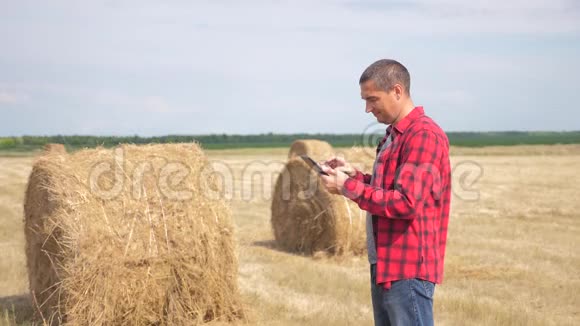 智慧农业生活方式理念一名农民工人在数字平板电脑上的田野里研究干草堆慢慢慢慢视频的预览图