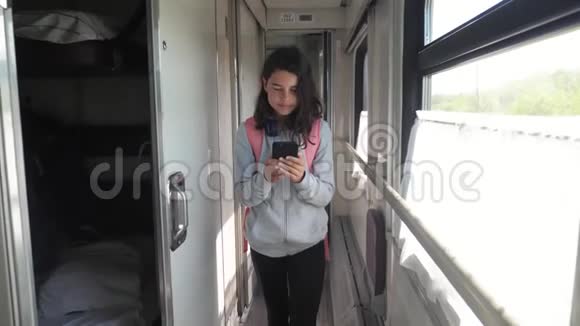 十几岁的女孩带着背包和智能手机在火车车厢里散步旅游运输铁路概念视频的预览图
