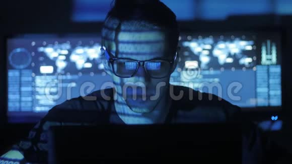 戴眼镜的黑客程序员正在电脑安全中心工作里面放满了显示屏视频的预览图