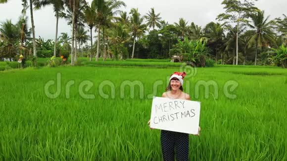 飞行无人机视频年轻女子与红色帽子和白板与手写文字圣诞快乐热带背景视频的预览图