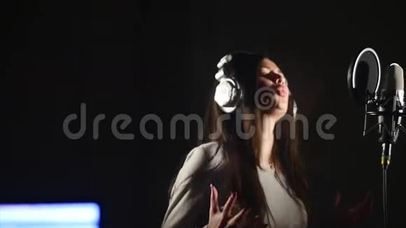 录音室带着耳机和录音室麦克风唱歌的女人视频的预览图