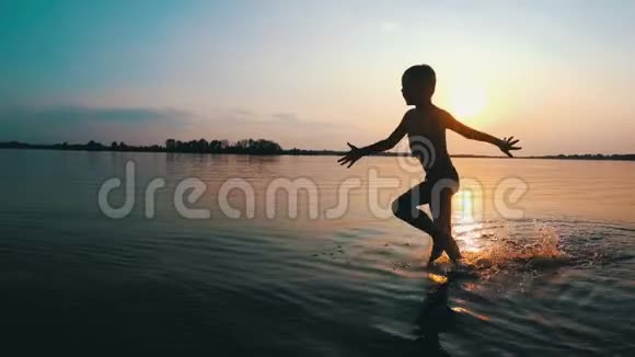 快乐男孩在日落时沿着海滩奔跑慢动作视频的预览图