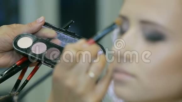 专业化妆师在金色卷发和蓝眼睛模型皮肤上涂上色调霜视频的预览图