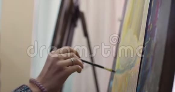 年轻的女艺术家在一个艺术工作室坐在一个Easel后面和画布上的绘画绘画过程艺术中视频的预览图