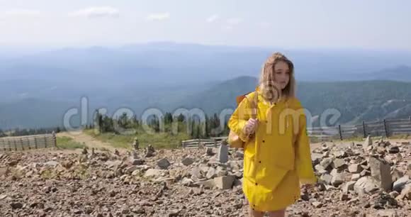 徒步旅行者背着背包在山顶徒步旅行穿着黄色雨衣的女孩在山顶上视频的预览图