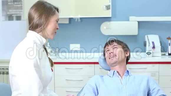 性格开朗的男性病人坐在牙科椅上与女性牙医交谈视频的预览图