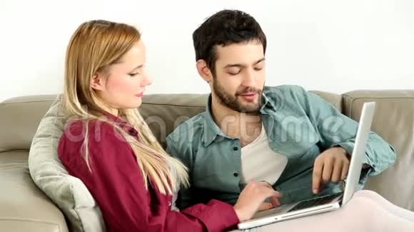 年轻夫妇坐在家里的笔记本电脑沙发上视频的预览图