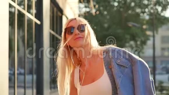 有魅力的年轻女性在耳机里听音乐在城市散步日落环顾四周微笑肖像视频的预览图