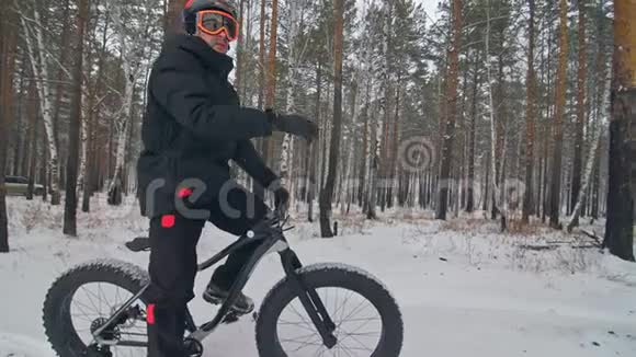 职业极限运动员骑自行车在户外坐一辆胖自行车骑自行车者在冬天的雪林中退缩与人同行视频的预览图