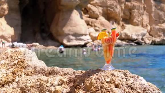 热带鲜鸡尾酒埃及海滩上的麦秆玻璃矗立在红海背景的岩石上视频的预览图