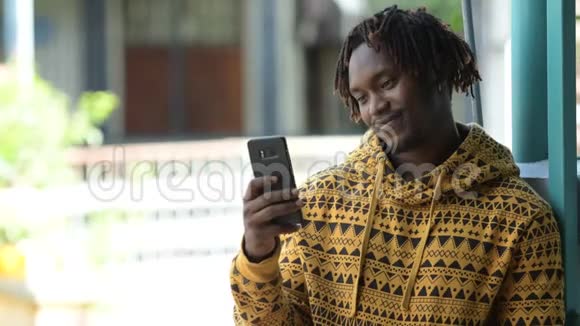年轻快乐英俊的非洲男人在户外大街上用电话微笑视频的预览图