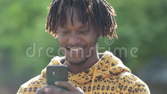 年轻快乐英俊的非洲男人在户外大街上用电话微笑视频的预览图