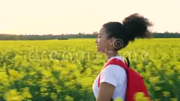非洲裔美国少女少女女青年背着红色背包在种子黄花地里徒步旅行视频的预览图