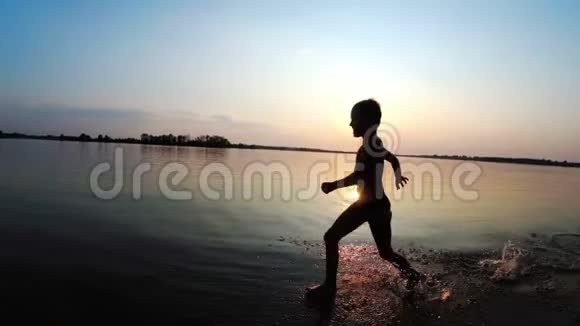 快乐的男孩在日落时沿着海滩奔跑慢动作视频的预览图