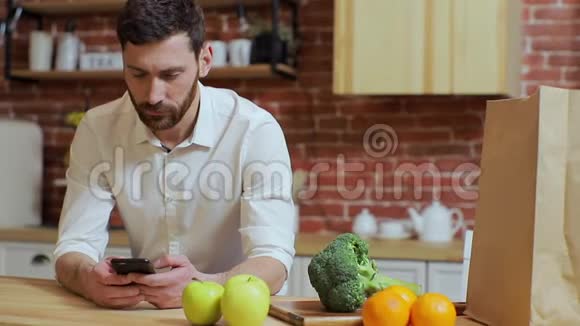 男人在家厨房用手机浏览帅哥浏览智能手机微笑快乐视频的预览图