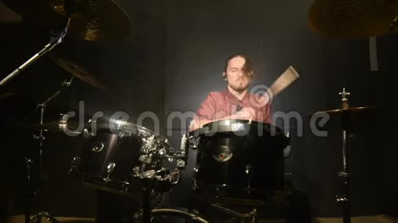 长发鼓手在黑色背景的黑暗房间里演奏鼓包摇滚音乐家静态计划宽角度视频的预览图
