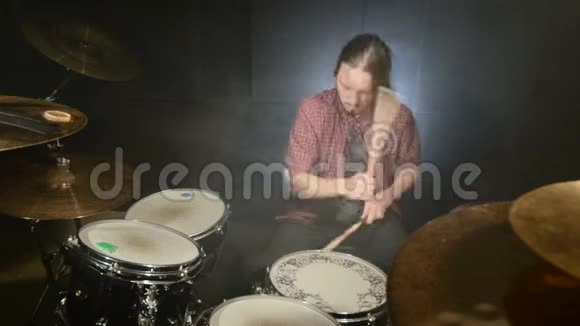 长发鼓手在黑色背景的黑暗房间里演奏鼓包摇滚音乐家静态计划宽角度视频的预览图