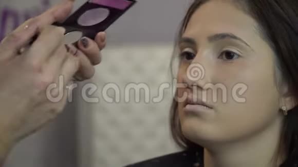美容院年轻漂亮的女孩模特坐在椅子上化妆师给女孩化妆化妆师视频的预览图