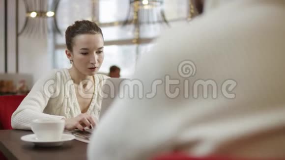 年轻女子在和一个男人坐在咖啡馆里用笔记本电脑工作视频的预览图