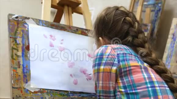 年轻可爱的女艺术家在一个艺术工作室坐在画架后面在画布上画画绘图过程视频的预览图