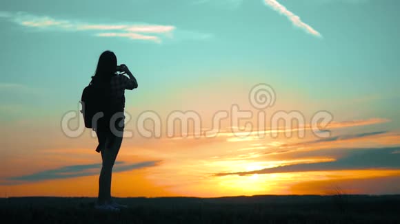 希普斯特的剪影女孩正在手机智能手机上拍摄美丽自然日落的视频视频的预览图
