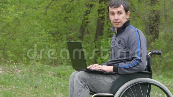 残疾人轮椅有一台坐在轮椅上的笔记本电脑工作在大自然的绿色环境中视频的预览图