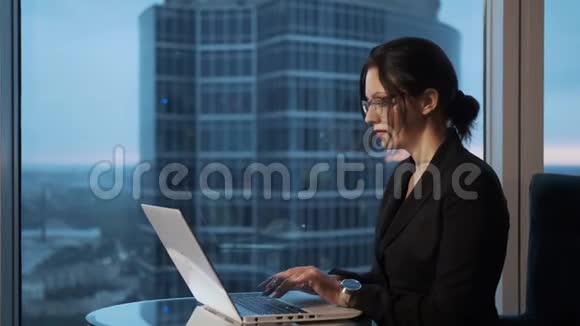 坐在办公室靠窗的手提电脑上工作的年轻女子视频的预览图