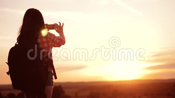 hipsterhiker生活方式剪影女孩正在手机智能手机上拍摄美丽自然日落的视频视频的预览图