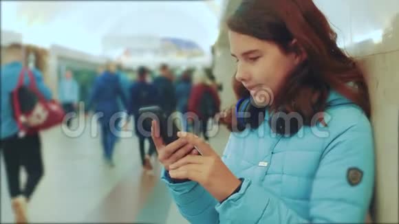 十几岁的女孩带着智能手机和耳机等待地铁很多人聚集在地下地铁地下工程视频的预览图