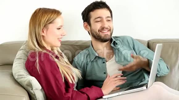 年轻夫妇坐在家里的笔记本电脑沙发上视频的预览图