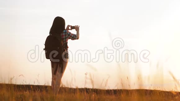 hipsterhiker剪影女孩正在手机智能手机上拍摄美丽自然日落的视频视频的预览图