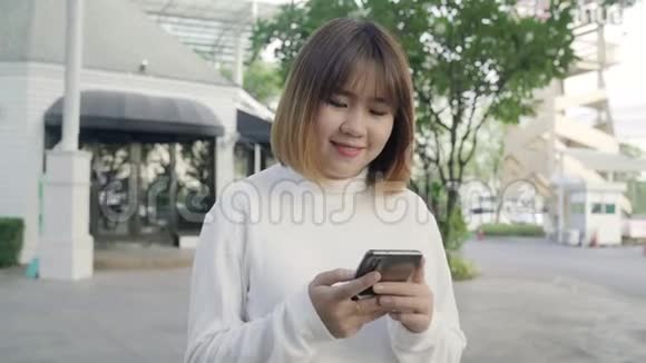 亚洲旅游博客女性晚上在市中心街头散步时在智能手机上使用触摸屏技术视频的预览图