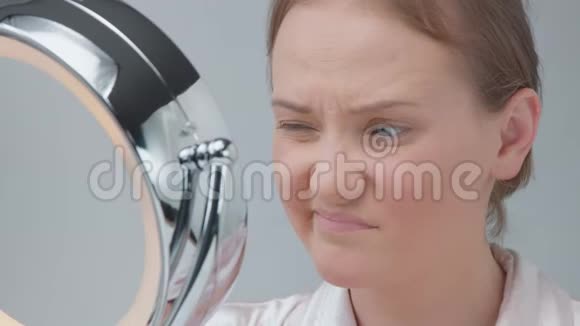 白种人女性带着没有化妆的带光镜检查她的皮肤并做面部护理视频的预览图
