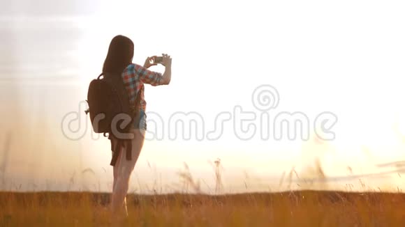 hipsterhiker剪影女孩正在手机智能手机上拍摄美丽自然日落的视频视频的预览图