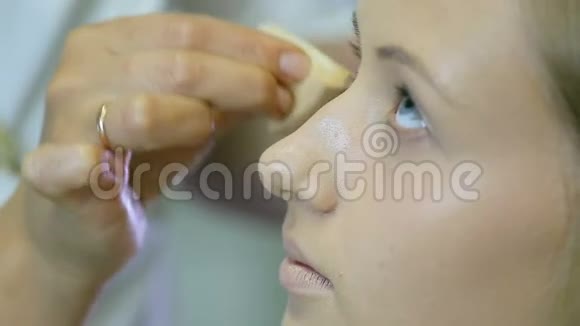 专业化妆师在金色卷发和蓝眼睛模型皮肤上涂上色调霜视频的预览图