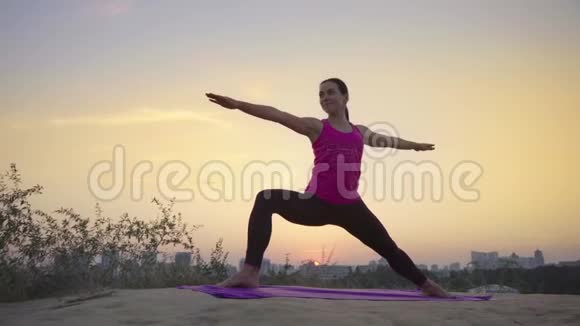 在大城市的背景下一位年轻女子在山上练习瑜伽视频的预览图
