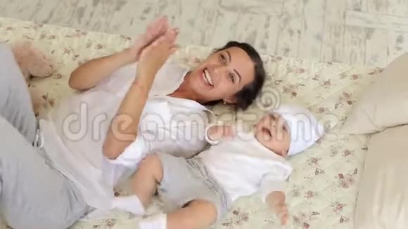 年轻快乐的妈妈正在床上卧室里和一个新生儿玩耍视频的预览图