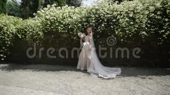 阳光明媚的一天年轻的新娘在鲜花旁边摆姿势视频的预览图