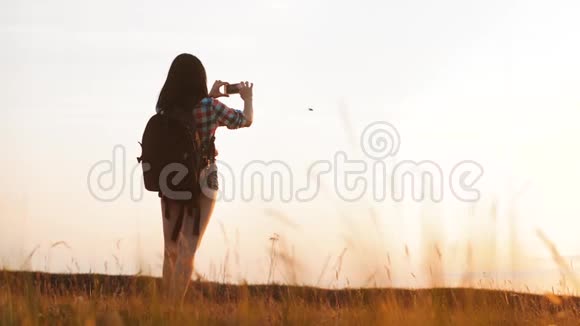 hipsterhiker剪影女孩正在手机智能手机上拍摄美丽自然日落的视频视频的预览图